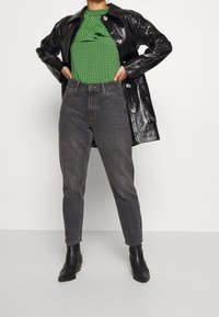 Black glossy leather coat over a green checkered top with ruffle detail, paired with high-waisted gray jeans and black ankle boots.