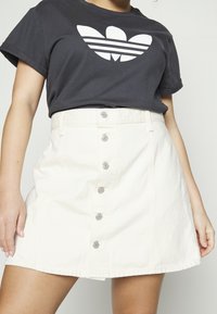 Biała spódnica dżinsowa o kształcie litery A, z guzikami z przodu i gładką fakturą. W połączeniu z czarnym t-shirtem z wyświetlanym logo.