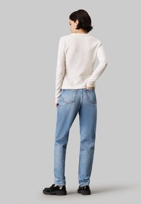 Top de punto de canalé en color crema de manga larga combinado con unos vaqueros de tiro alto en azul claro, con un corte relajado y perneras rectas, llevados con zapatos de plataforma negros.
