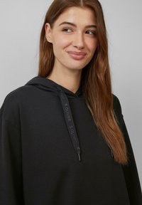 Schwarz sweatshirt mit Kapuze aus weichem Stoff. Verfügt über verstellbare Kordeln mit Logo-Details und eine entspannte Silhouette.