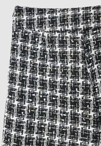 Tissu tissé noir et blanc avec une finition texturée, présentant un motif à carreaux et des fils dorés entrelacés.