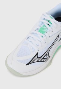 White athletic shoe with mesh fabric, black zigzag design, and mint green accent. Features round toe, laces, and textured sole.