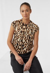 Kurzarm-Bluse mit Leopardenmuster in Beige, Braun und Schwarz. Der Stoff hat eine glatte Textur und einen gerafften Halsausschnitt. Kombiniert mit schwarzen Hosen.