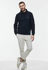 Námořnická mikina s kapucí z jemné tkaniny, s malým logem. V kombinaci se světle béžovými kalhotami a béžovými teniskami se šedými akcenty.