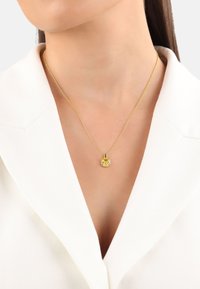 Collarín blanco con un collar de oro que tiene un colgante redondo con una gema amarilla central rodeada de acentaciones blancas.