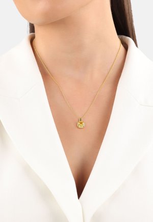 Collarín blanco con un collar de oro que tiene un colgante redondo con una gema amarilla central rodeada de acentaciones blancas.