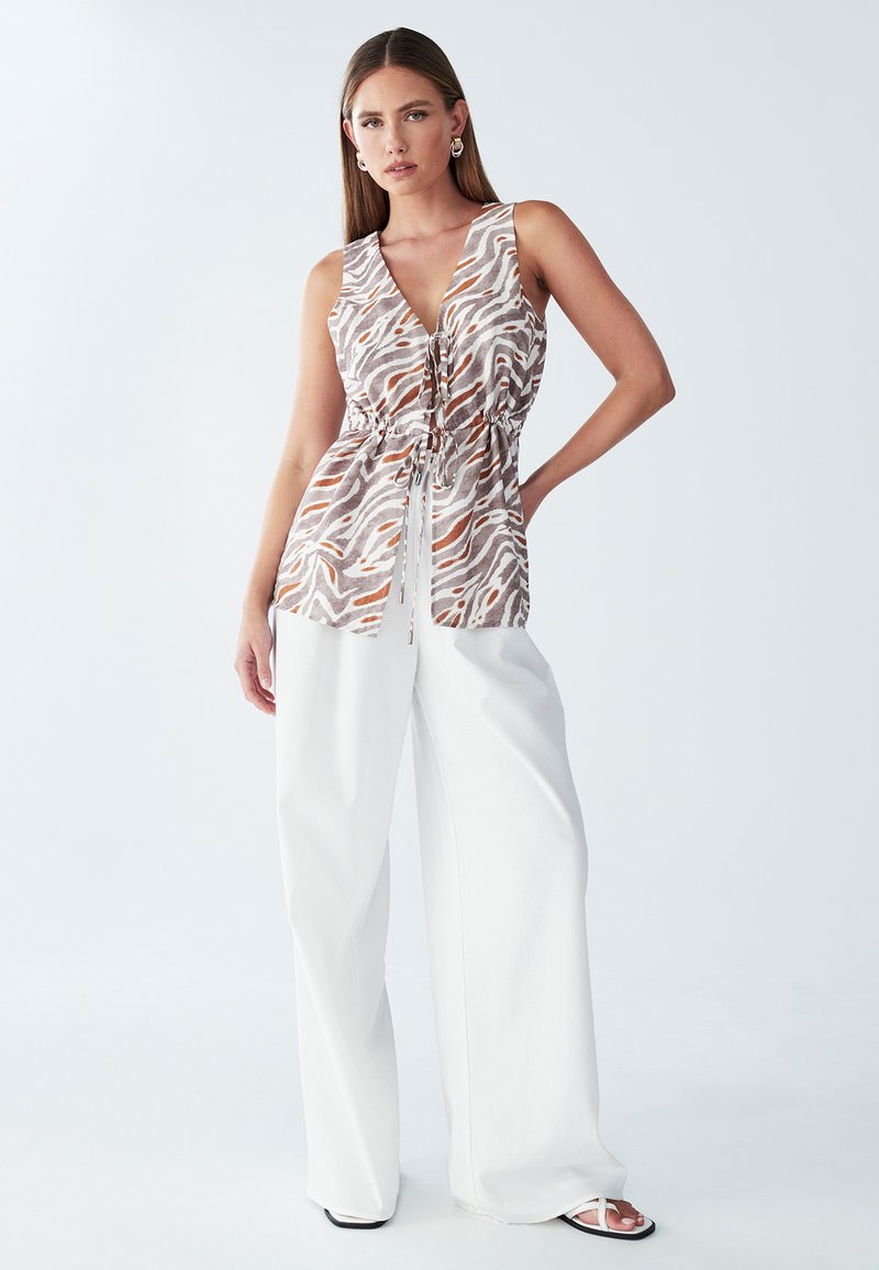 Ärmløs top med et hvidt, brunt og orange abstrakt mønster, der har en snoreliv, parret med hvide bukser med brede ben.