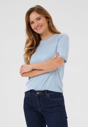Helles, hellblaues Kurzarmoberteil aus weichem Material mit rundem Halsausschnitt. Kombiniert mit dunkelblauen Jeans im klassischen Schnitt.