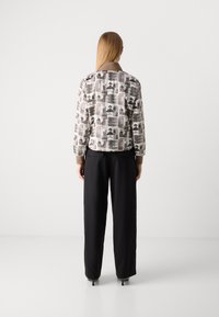 Giacca bomber stampata in beige con motivi astratti neri. Collo marrone, maniche lunghe, abbinata a pantaloni neri a gamba larga. Tessuto morbido.