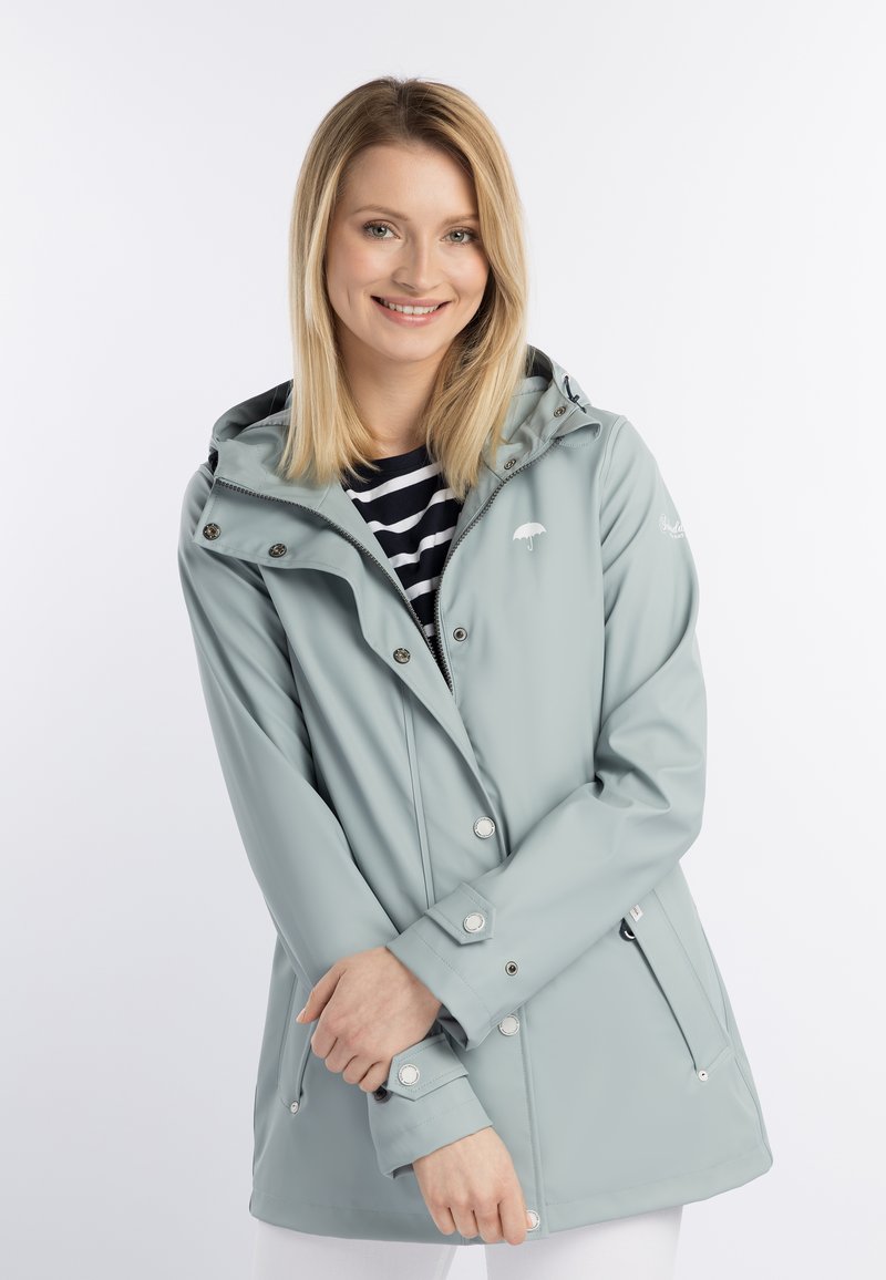 Ljusblå regnjacka med huva, tryckknappar och fickor med dragkedja. Mjuk, slät textur med en liten paraplylogotyp på bröstet.