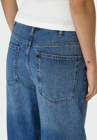 Svijetloplave traperice imaju opuštenu siluetu, dva stražnja džepa i vidljivo šivanje duž šavova. Tkanina ima izblijedjeli izgled.