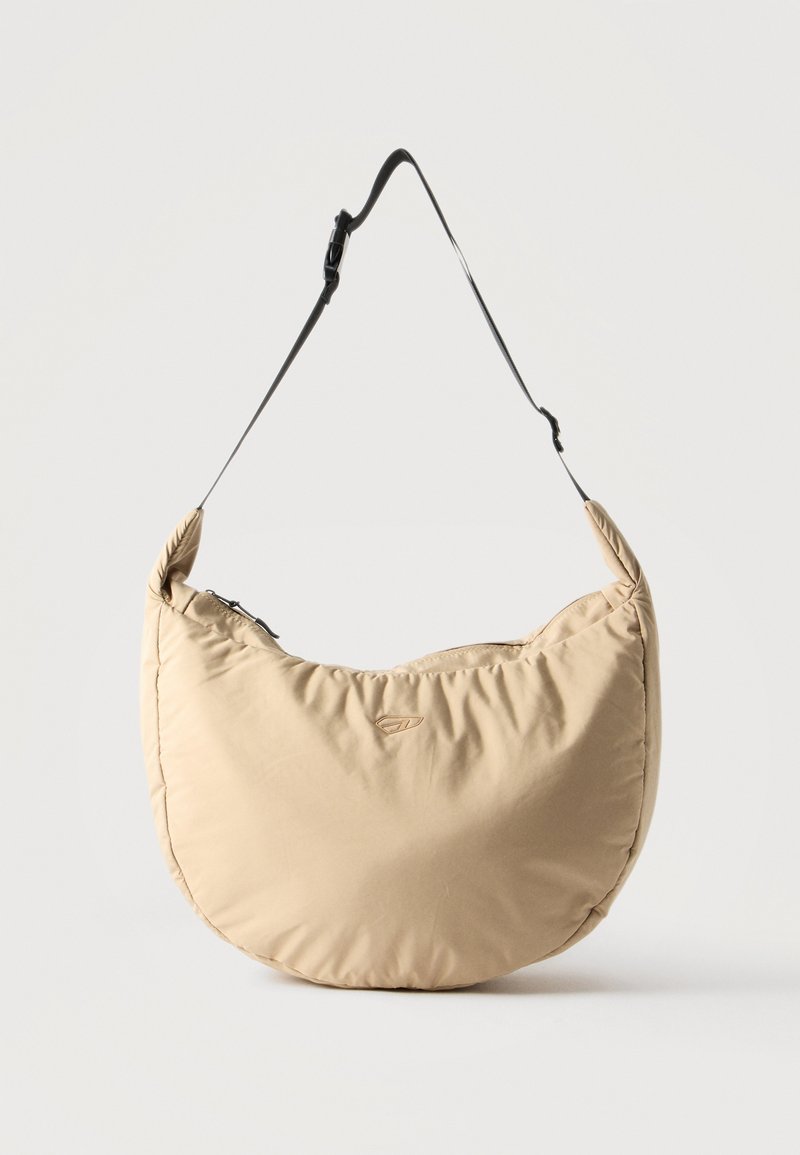 Μπεζ τσάντα ώμου σε σχήμα ημισελήνου με μαύρο ρυθμιζόμενο ιμάντα και επάνω φερμουάρ, σε απλό λευκό φόντο.