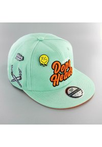 Mint green cap featuring embroidered "Dope Heads" text in orange, cross-patterned graphic, and several colorful patches. Flat bill design.