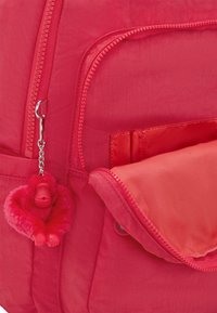 Röd nylonryggsäck med ett zip-lock fag, en plyschapa nyckelring och en slät yta på framfickan.