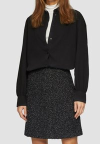 Camicia nera con bottoni e maniche lunghe, abbinata a una gonna nera con texture caratterizzata da un motivo puntinato. Entrambi i capi hanno una vestibilità rilassata.