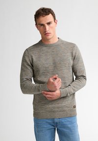 Maglione lavorato a maglia con texture in tonalità tenui di grigio e blu, scollo rotondo, polsini e orlo a costine. Indossato con jeans azzurri.