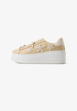 Beige platensneaker met geweven textuur, versierd met parel- en kralenbloemmotieven, witte veters en een dikke witte zool.