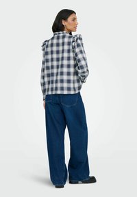 Hvid og marineblå ternet skjorte med flæset skulderdetaljer, parret med løstsiddende blå denimjeans og sorte chunky sko.