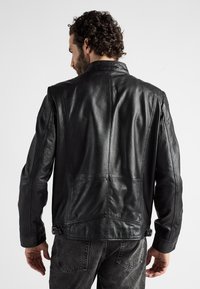 Zwarte leren jas met een gestructureerd ontwerp, voorzien van een verhoogde kraag, schouderaccenten en textuurpanelen. De achterkant toont de stiksels.