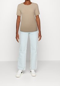 T-shirt beige a coste con maniche corte, abbinato a jeans dritti azzurri chiari e sneakers bianche con dettagli neri.