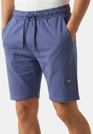 Homme portant un short bleu à cordon de serrage avec des poches latérales et un petit logo "Lee Cooper" noir et blanc sur la jambe gauche.