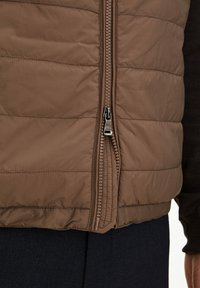 Braune gesteppte Weste aus glattem, leichtem Material. Verfügt über einen durchgehenden Reißverschluss und eine taillierte Passform mit horizontalen Nähten.