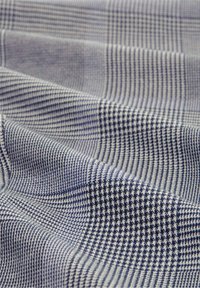 Tissu à carreaux bleu et blanc avec un motif de petits et grands pied-de-poule et motifs en grille, présenté avec des plis et des détails de texture.