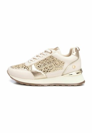 Zapatillas beige con acentos metálicos dorados, paneles de malla y superposiciones texturizadas; suela acolchada con un leve tacón y una lengüeta en la parte trasera.