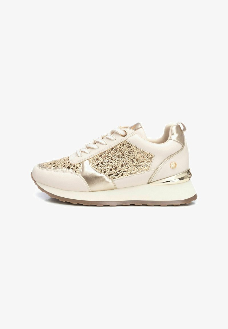 Zapatillas beige con acentos metálicos dorados, paneles de malla y superposiciones texturizadas; suela acolchada con un leve tacón y una lengüeta en la parte trasera.