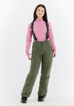 Lichte roze lange mouw top en groene skibroek met verstelbare zwarte bretels. De broek heeft een gladde textuur en een ontspannen pasvorm.