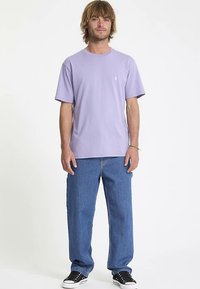 Lavender cotton t-shirt with short sleeves and a round neckline, paired with loose blue denim jeans and black sneakers.