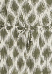 Tkanina w zielono-białe wzory z oliwkowozielonym abstrakcyjnym wzorem kropek oraz ściągaczem wiązanym w pasie.