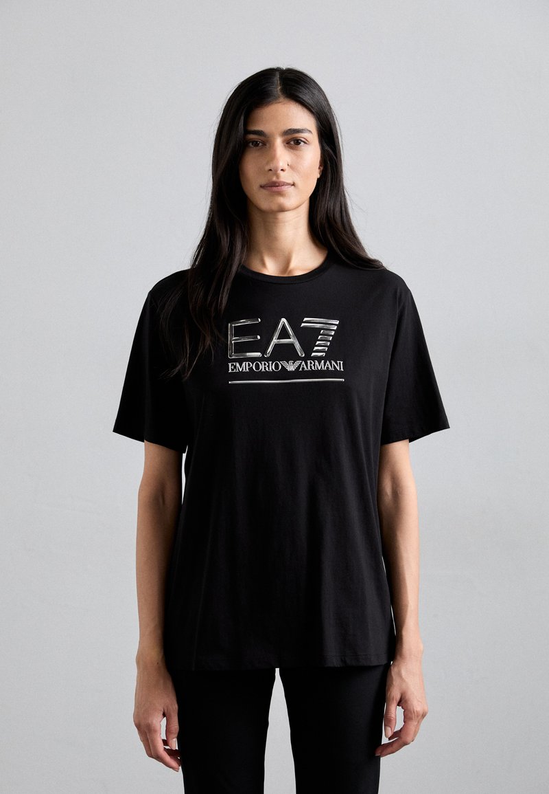 Melna kokvilnas T-krekls ar metāliski sudraba logotipu "EA7 EMPORIO ARMANI" uz priekšu. Īsas piedurknes un vaļīga piegriezums. Vienkārša tekstūra.