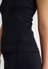 Top da donna nero a costine, dal design aderente, con scollatura a barca e dettagli di orlo cuciti, realizzato in tessuto elasticizzato per una vestibilità aderente.