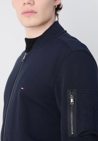 Jūras spēku bumbvedēja jaka ar rāvējslēdzēju priekšā, ribotām apkaklēm un rāvējslēdzēja kabatu uz piedurknes. Izgatavota no gludas auduma ar pieguļošu dizainu.