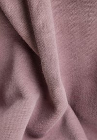 Měkká, skládáná tkanina v jemné mauve s jemnou, hladkou pletenou strukturou a subtilními detaily světla a stínu.