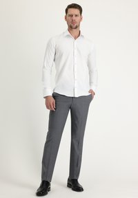 Camisa blanca de manga larga, de corte ajustado. Pantalones grises de traje, de tejido suave, con una textura sutil, completados con zapatos de vestir negros.