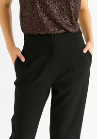 Black high-waisted trousers with a smooth, textured fabric, featuring side pockets and a sharp pleat detail.