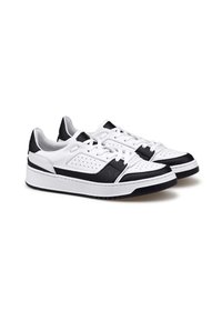 Un paio di sneaker bianche basse con accenti neri, dettagli perforati, lacci bianchi e suole bianche spesse su uno sfondo bianco.