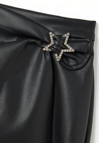 Tessuto plissettato in pelle nera con una fibbia decorativa a forma di stella in strass che tiene insieme il materiale arricciato.