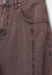 Tessuto di denim rosa con finitura testurizzata, dotato di tasche frontali, chiusura con bottone e cuciture a contrasto lungo le cuciture.
