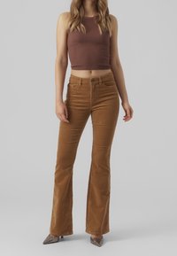 Brown corduroy flared pants with a high waist, featuring front pockets and a smooth texture. Paired with a fitted brown ribbed top.