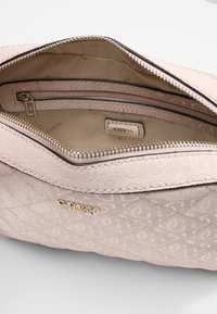 Interno di borsa a tracolla trapuntato color rosa chiaro con fodera con marchio, scomparti con zip e dettagli in metallo dorato.