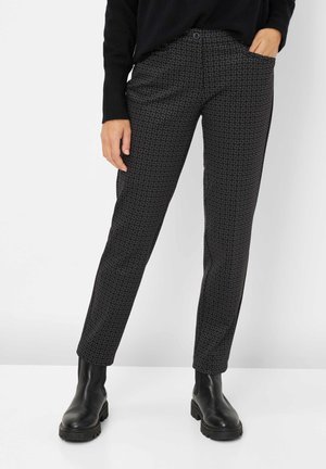 Black patterned trousers featuring a geometric design, slim fit, side pockets, and paired with black ankle boots.