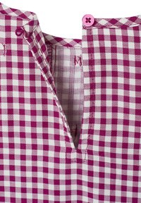 Karomusterstoff in Magenta und Weiß, mit einem V-Ausschnitt und pinken Knopfdetails am Kragen. Material aus Baumwollmischung.