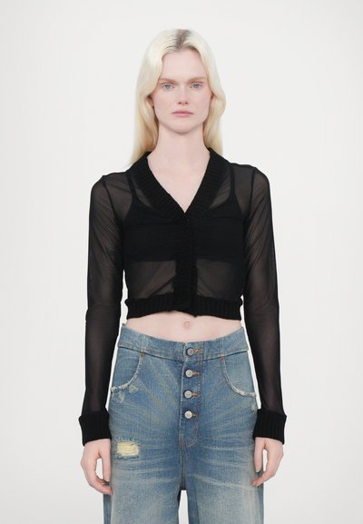 Sort cropped cardigan i mesh stof med tekstureret ribstrik ved halsen og manchetterne, båret over højtaljede slidte blå gedinsim jeans.
