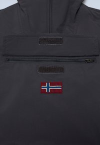 Mörkgrå jacka med en framfickan med dragkedja, med en norsk flagga på och två kardborreband på den övre delen av ryggen för justeringar.