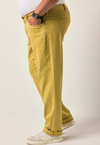 Žluté bavlněné kalhoty s rovný střihem, jemnou texturou a bočními kapsami, doplněné bílými a šedými teniskami.