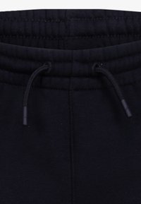 Schwarze Sweatpants mit einem Kordelzugbund, aus weichem Stoff. Sichtbare Nähte entlang des Oberteils und verstärkte Ösen für den Kordelzug.