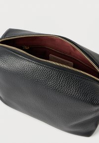 Sort læderpung med tekstureret finish, guldlynlås og bordeaux indre. Den er rektangulær med en blød struktur, velegnet til tilbehør.